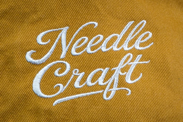 マスタード色の生地に白糸で施したスクリプト刺繍